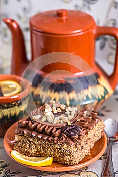 Delicious and sweet chocolate cake with cream and nuts and a Ñup of black tea with lemon. tea set with teapot, saucer and Ñup